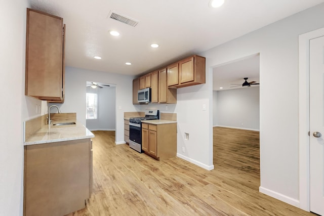 kitchen with light stone countertops, appliances with stainless steel finishes, ceiling fan, sink, and light hardwood / wood-style floors