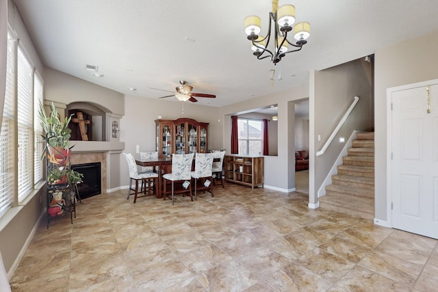 dining space featuring ceiling fan with notable chandelier and a tiled fireplace