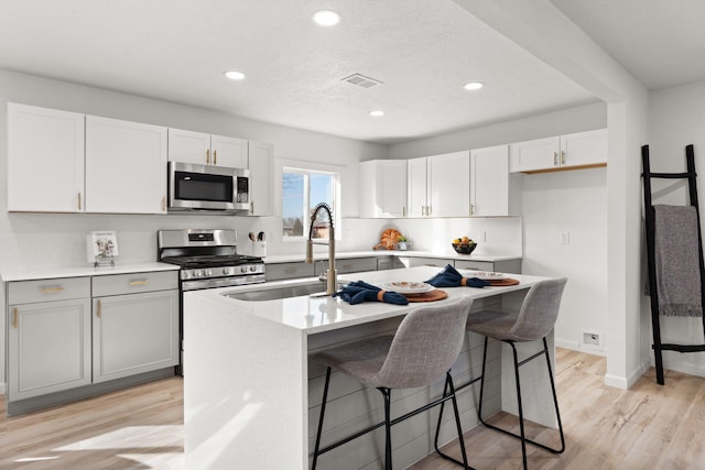 kitchen featuring white cabinets, sink, light hardwood / wood-style flooring, an island with sink, and stainless steel appliances