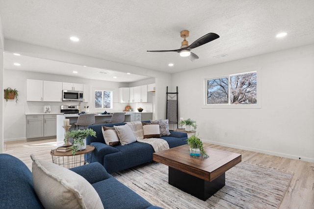 living room with ceiling fan, a textured ceiling, and light wood-type flooring