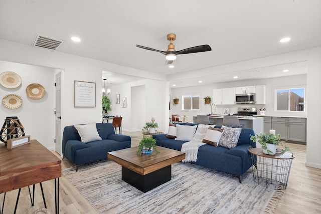 living room with ceiling fan with notable chandelier, light hardwood / wood-style flooring, and sink