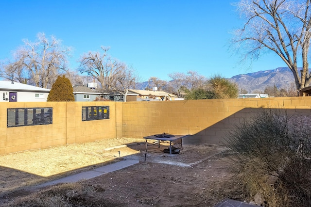 view of yard featuring an outdoor fire pit, a fenced backyard, and a mountain view