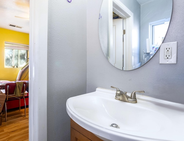 bathroom with a textured wall, visible vents, a sink, and wood finished floors