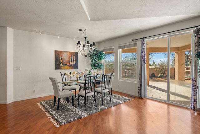 dining area featuring a textured ceiling, wood finished floors, baseboards, an inviting chandelier, and track lighting