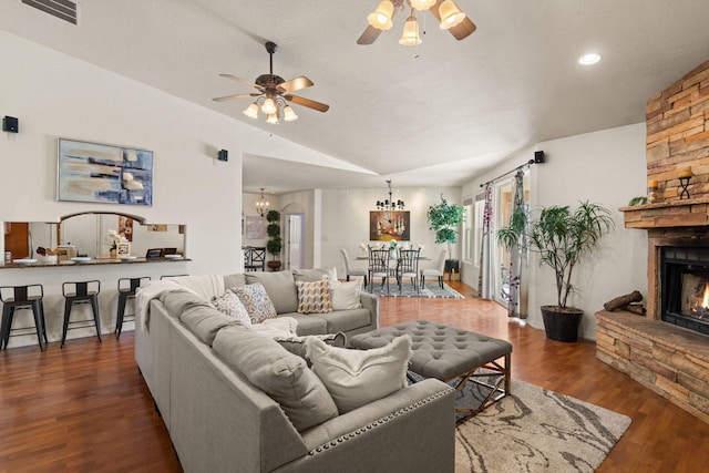 living area featuring lofted ceiling, ceiling fan with notable chandelier, a fireplace, wood finished floors, and visible vents