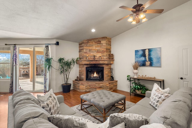 living room with wood finished floors, ceiling fan, vaulted ceiling, a stone fireplace, and a textured ceiling