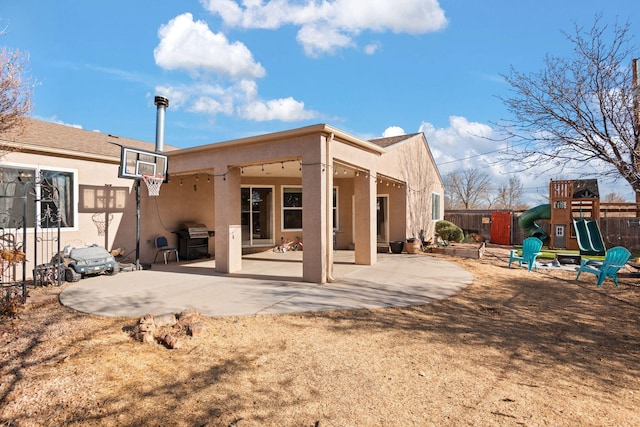 rear view of house with a patio area, a playground, fence, and stucco siding