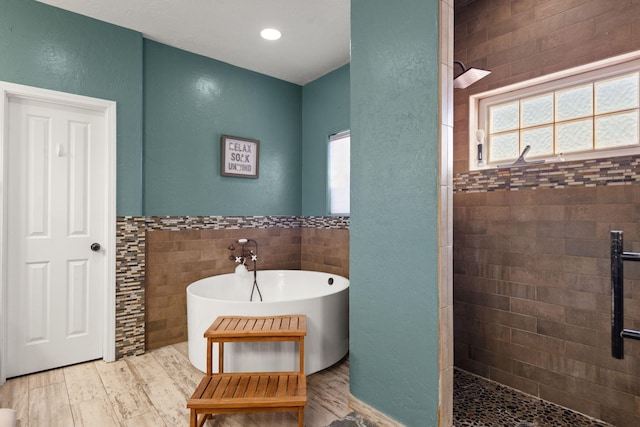 full bath with a healthy amount of sunlight, tiled shower, a soaking tub, and tile walls