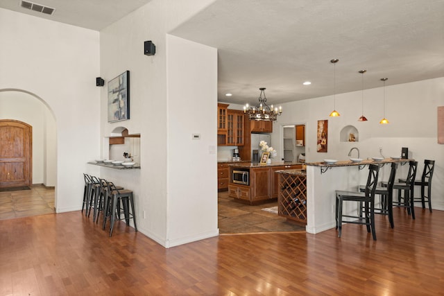 kitchen with arched walkways, a breakfast bar, visible vents, appliances with stainless steel finishes, and brown cabinets