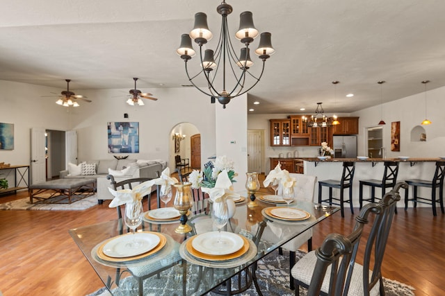 dining space featuring arched walkways, ceiling fan with notable chandelier, wood finished floors, and recessed lighting