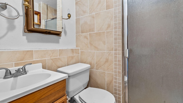 bathroom with vanity, toilet, a shower with door, and tile walls