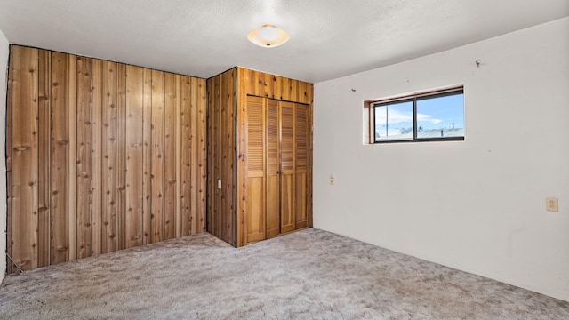 carpeted spare room featuring a textured ceiling and wood walls