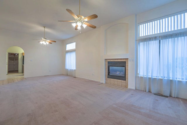 unfurnished living room featuring a tile fireplace, light carpet, ceiling fan, and high vaulted ceiling