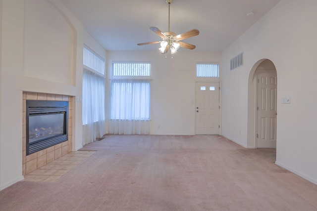 unfurnished living room with ceiling fan, light colored carpet, a towering ceiling, and a fireplace