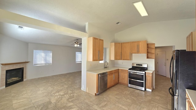 kitchen featuring ceiling fan, sink, stainless steel appliances, lofted ceiling, and a tiled fireplace