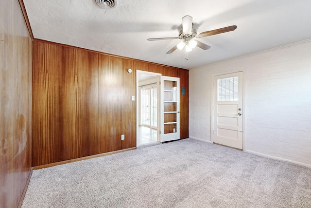 empty room with wooden walls, ceiling fan, light carpet, and ornamental molding