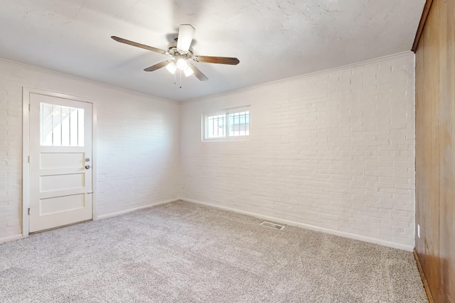 carpeted empty room featuring ceiling fan, crown molding, and brick wall