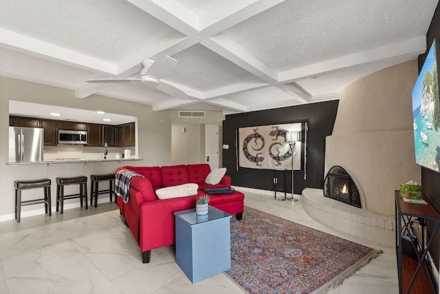 living room with a fireplace, coffered ceiling, a textured ceiling, ceiling fan, and beamed ceiling