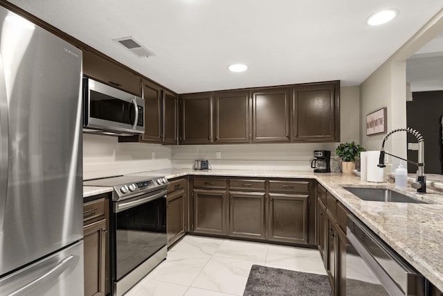 kitchen with dark brown cabinetry, stainless steel appliances, light stone counters, and sink