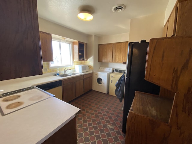 kitchen with sink, backsplash, stainless steel dishwasher, washing machine and clothes dryer, and cooktop