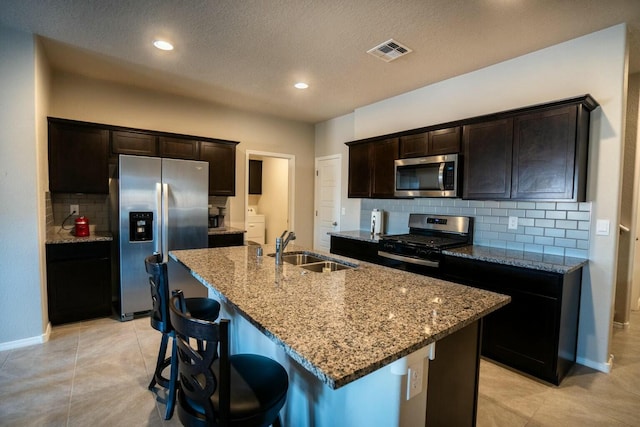 kitchen featuring light stone countertops, stainless steel appliances, an island with sink, sink, and light tile patterned floors