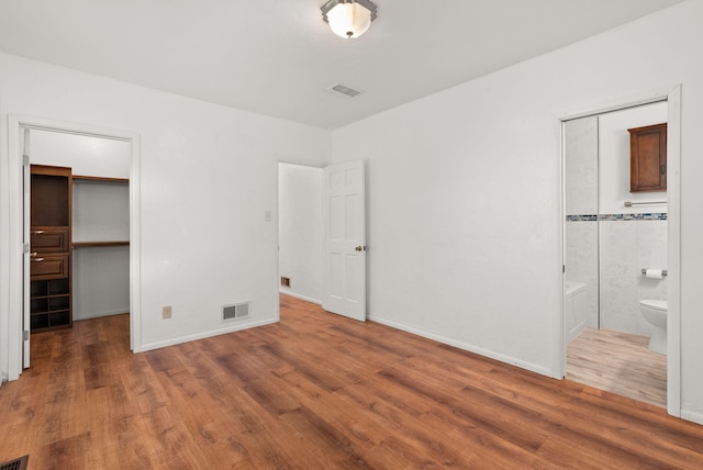 unfurnished bedroom with a walk in closet, ensuite bathroom, a closet, and dark wood-type flooring