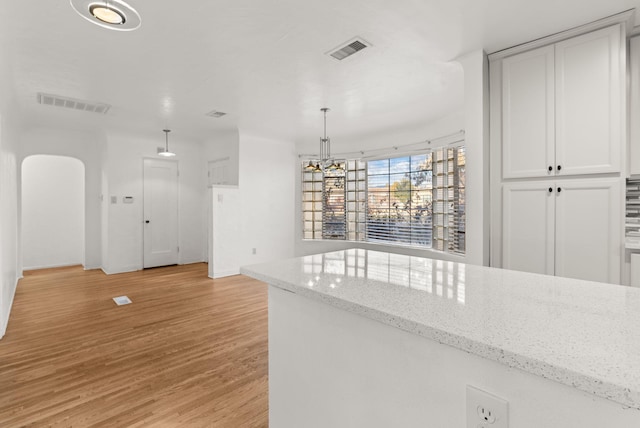 kitchen with light stone countertops, light wood-type flooring, decorative light fixtures, and white cabinetry