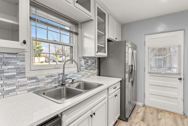 kitchen with light wood-type flooring, backsplash, stainless steel appliances, sink, and white cabinets