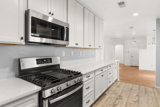 kitchen with white cabinets, hanging light fixtures, light wood-type flooring, appliances with stainless steel finishes, and light stone counters