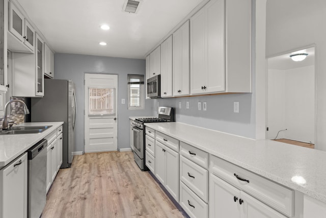 kitchen featuring white cabinets, sink, light hardwood / wood-style flooring, appliances with stainless steel finishes, and light stone counters