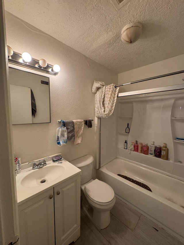 bathroom with toilet, vanity, bathtub / shower combination, a textured wall, and a textured ceiling