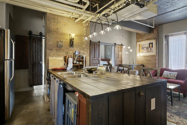 kitchen featuring a barn door, stainless steel fridge, sink, and brick wall