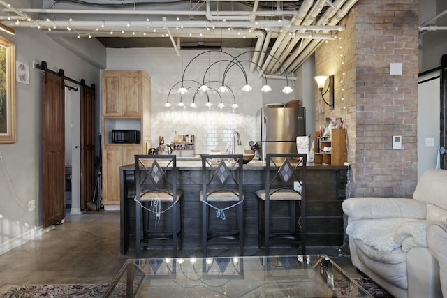 bar with light brown cabinets, a barn door, stainless steel refrigerator, and brick wall