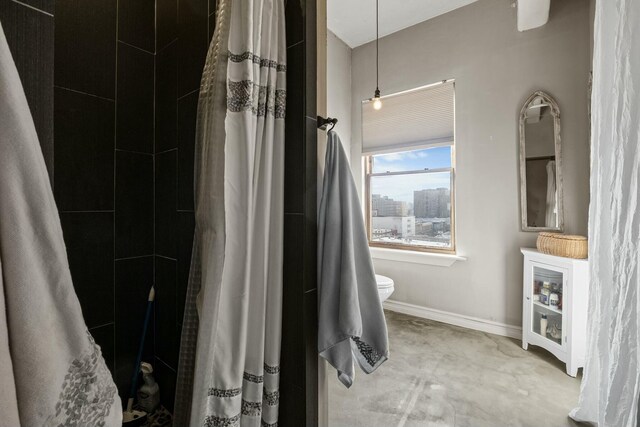 bathroom with concrete flooring, a shower with shower curtain, and toilet