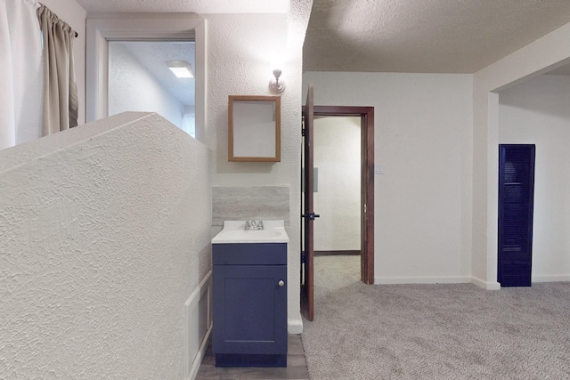 corridor with light carpet, a textured ceiling, and sink