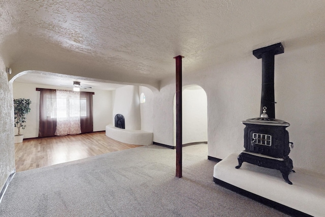 unfurnished living room with carpet flooring, a wood stove, and a textured ceiling