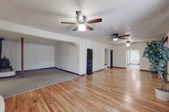 unfurnished living room featuring a wood stove, ceiling fan, a textured ceiling, and light wood-type flooring