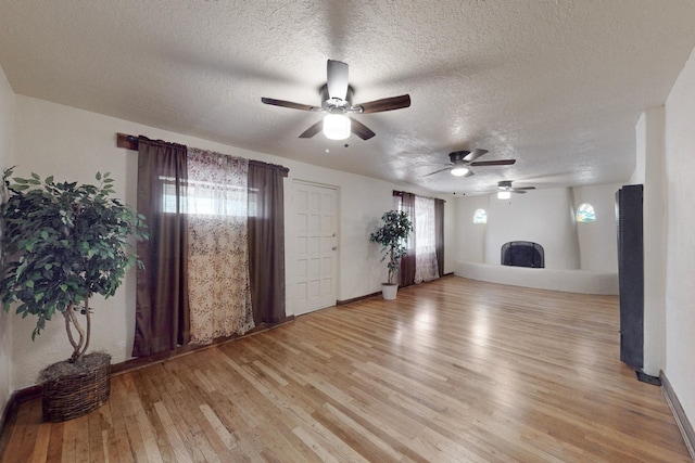 unfurnished living room featuring ceiling fan, light hardwood / wood-style floors, and a textured ceiling