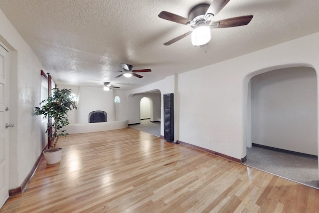 living room with a textured ceiling, a large fireplace, light hardwood / wood-style flooring, and ceiling fan