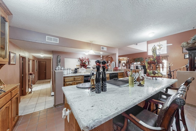 kitchen with a kitchen breakfast bar, a textured ceiling, a kitchen island, hanging light fixtures, and light tile patterned flooring