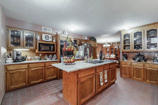 kitchen with tile patterned flooring, a kitchen island, a chandelier, and appliances with stainless steel finishes