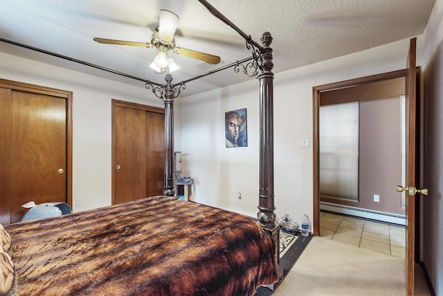 bedroom featuring tile patterned floors, a textured ceiling, baseboard heating, ceiling fan, and multiple closets