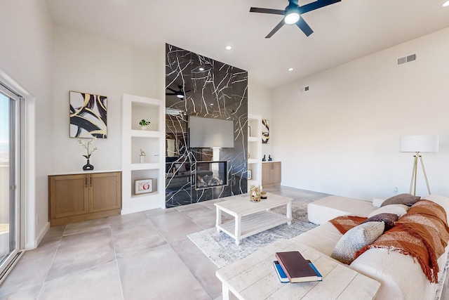 living room featuring built in shelves, ceiling fan, a fireplace, and a baseboard heating unit