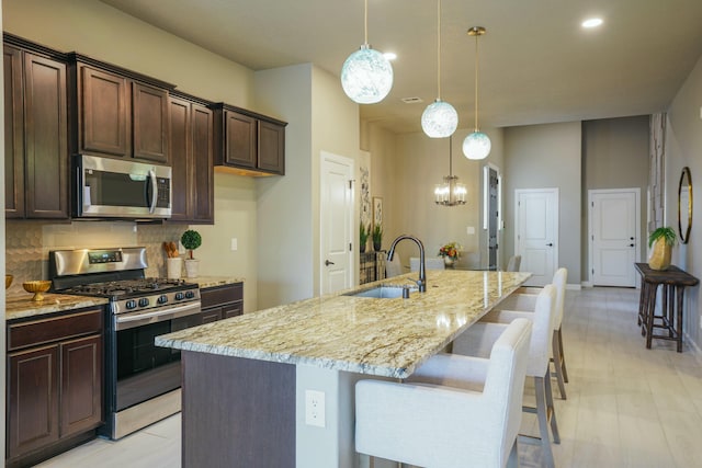 kitchen with a center island with sink, sink, hanging light fixtures, decorative backsplash, and stainless steel appliances