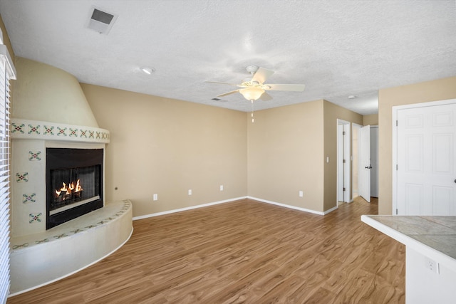 unfurnished living room with ceiling fan, a large fireplace, a textured ceiling, and light hardwood / wood-style flooring