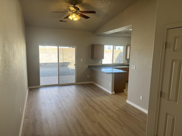 interior space with kitchen peninsula, a textured ceiling, vaulted ceiling, ceiling fan, and light hardwood / wood-style flooring