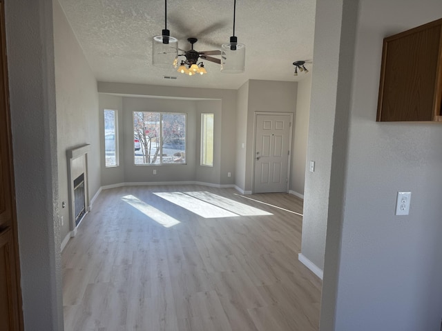 unfurnished living room featuring ceiling fan, light hardwood / wood-style floors, and a textured ceiling