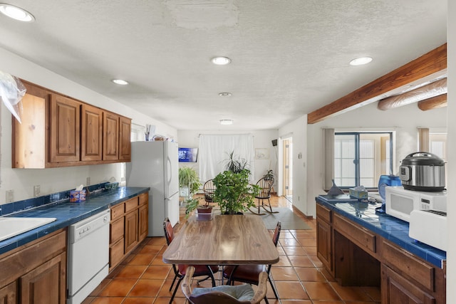 kitchen featuring beam ceiling, sink, a textured ceiling, white appliances, and dark tile patterned flooring