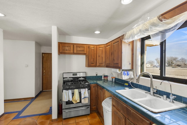 kitchen featuring gas stove, tile counters, sink, a textured ceiling, and light tile patterned floors