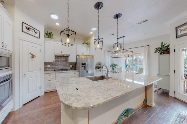 kitchen with stainless steel appliances, sink, decorative light fixtures, a center island with sink, and white cabinets